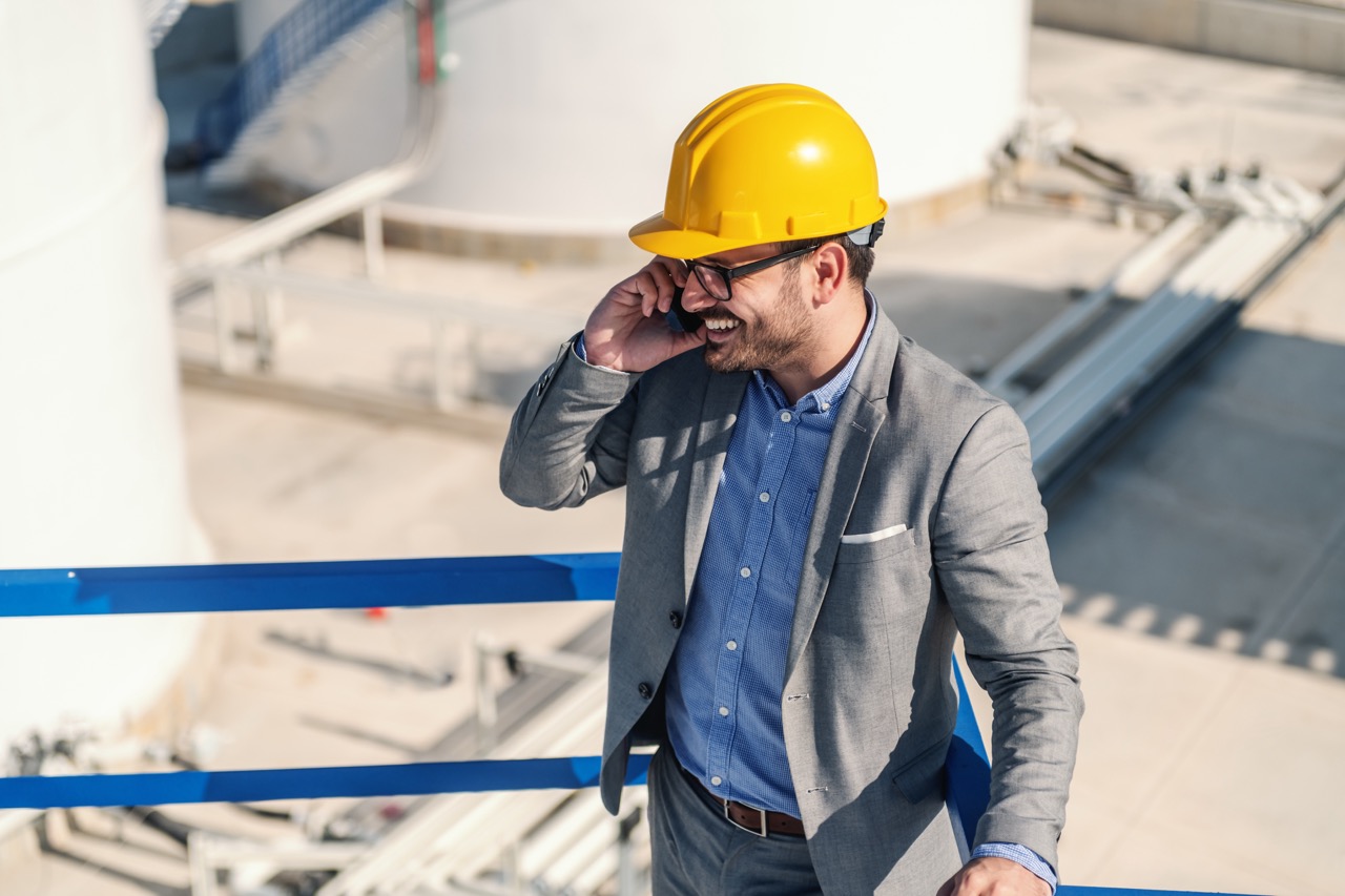 Young smiling attractive caucasian multimillionaire standing on the stairs and having a phone call. Refinery exterior.